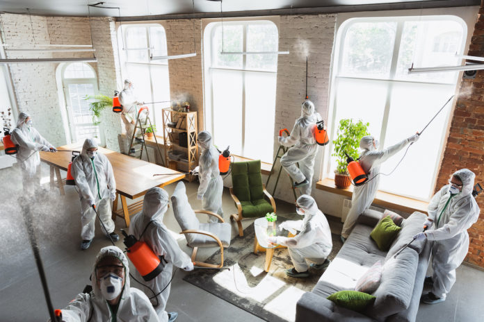 Coronavirus Pandemic. A disinfectors in a protective suit and mask sprays disinfectants in the house or office