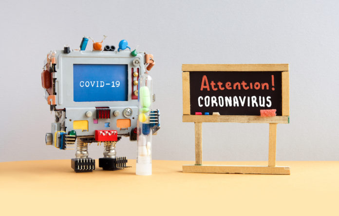 Attention coronavirus covid 19. A robotic research computer doctor holds a test tube with drugs and pills. Black chalkboard with the handwritten words warning of an epidemiological virus threat.